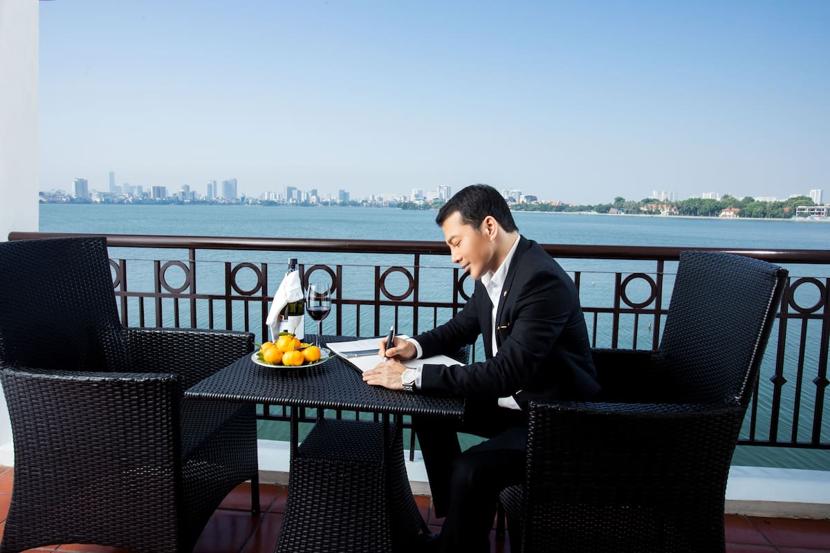 A man in a suit writing at a table with a city skyline view.