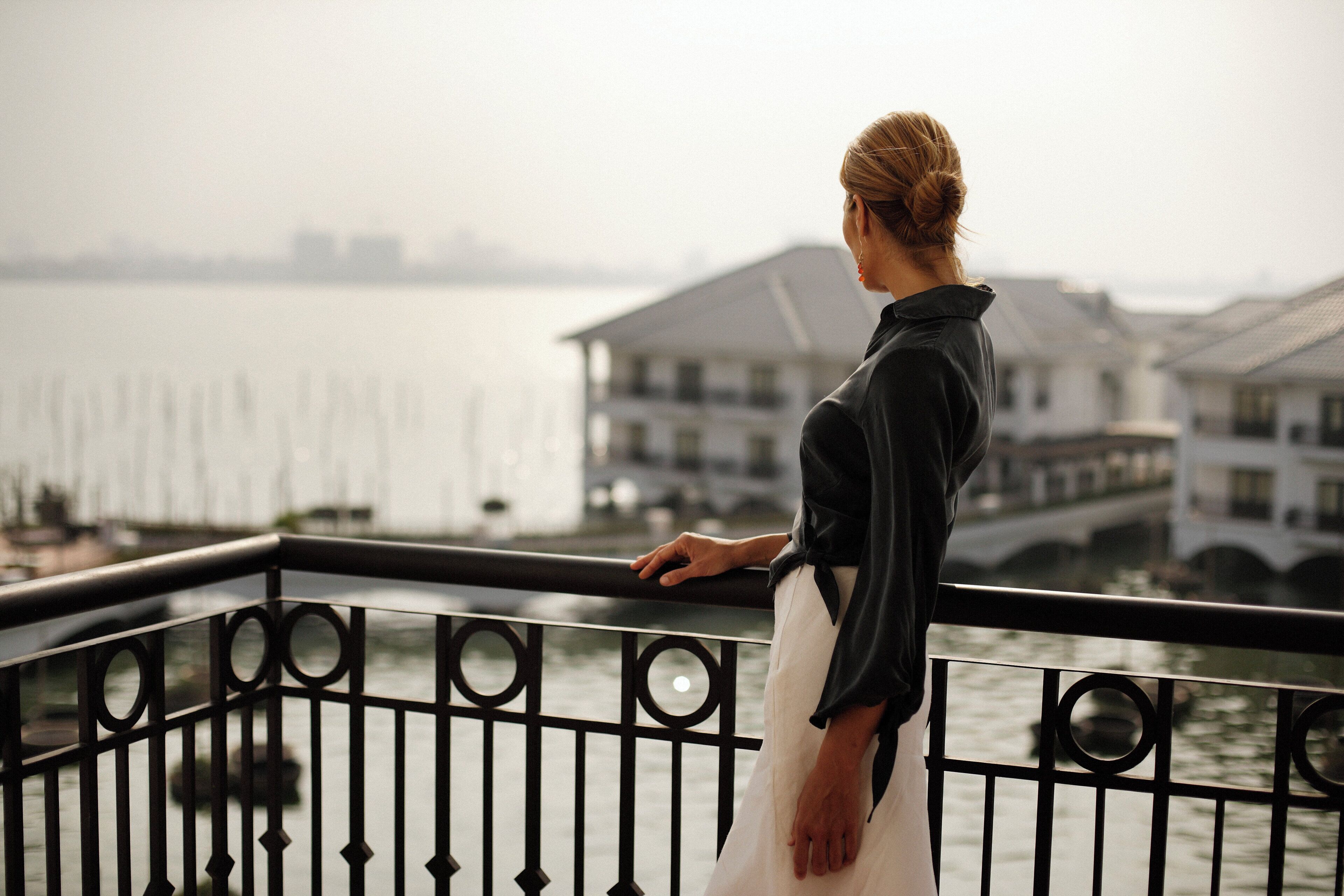 A person standing on a balcony overlooking a body of water with buildings in the background.