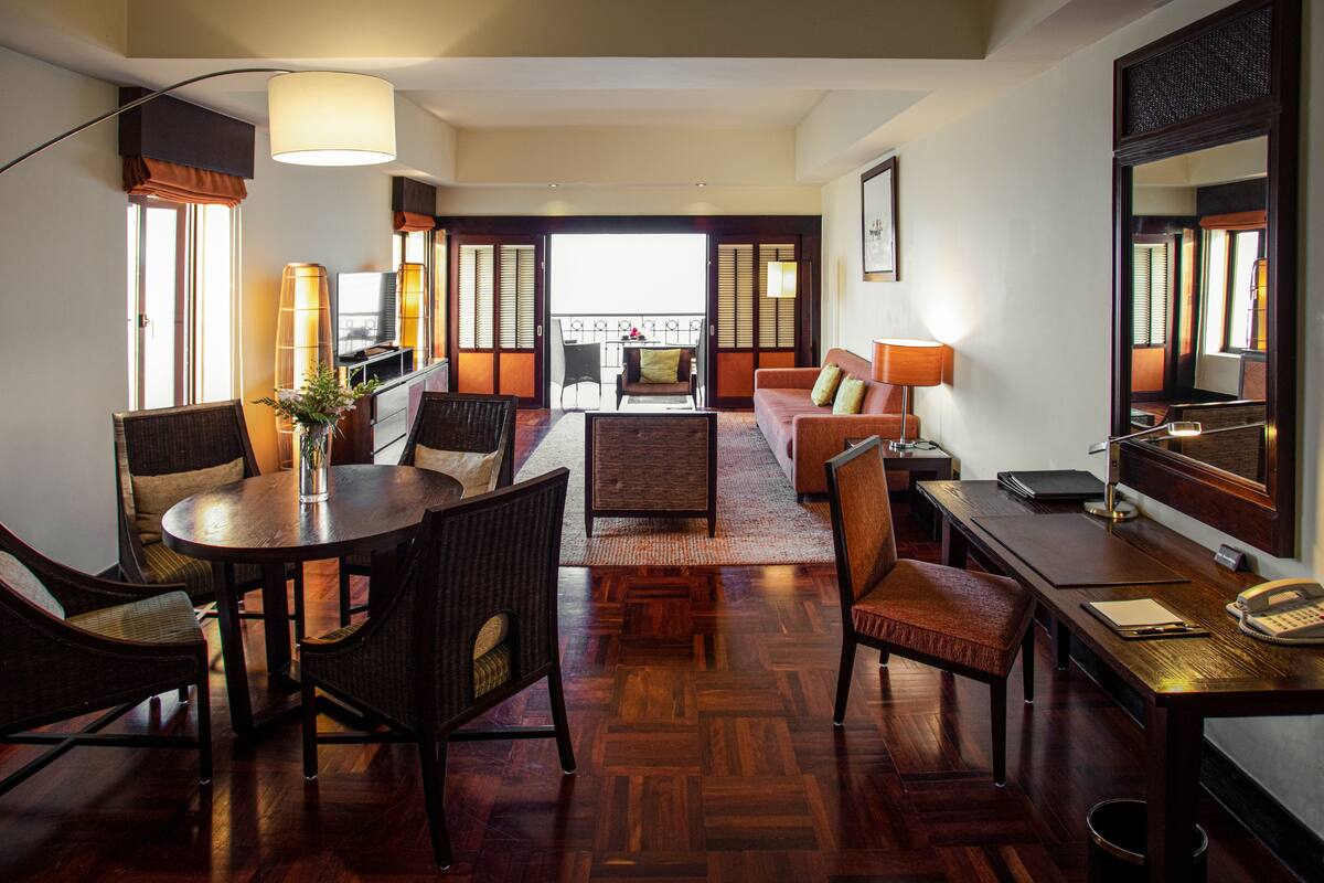 A hotel room with a dining area, a sofa, a desk with a telephone, and a large mirror.