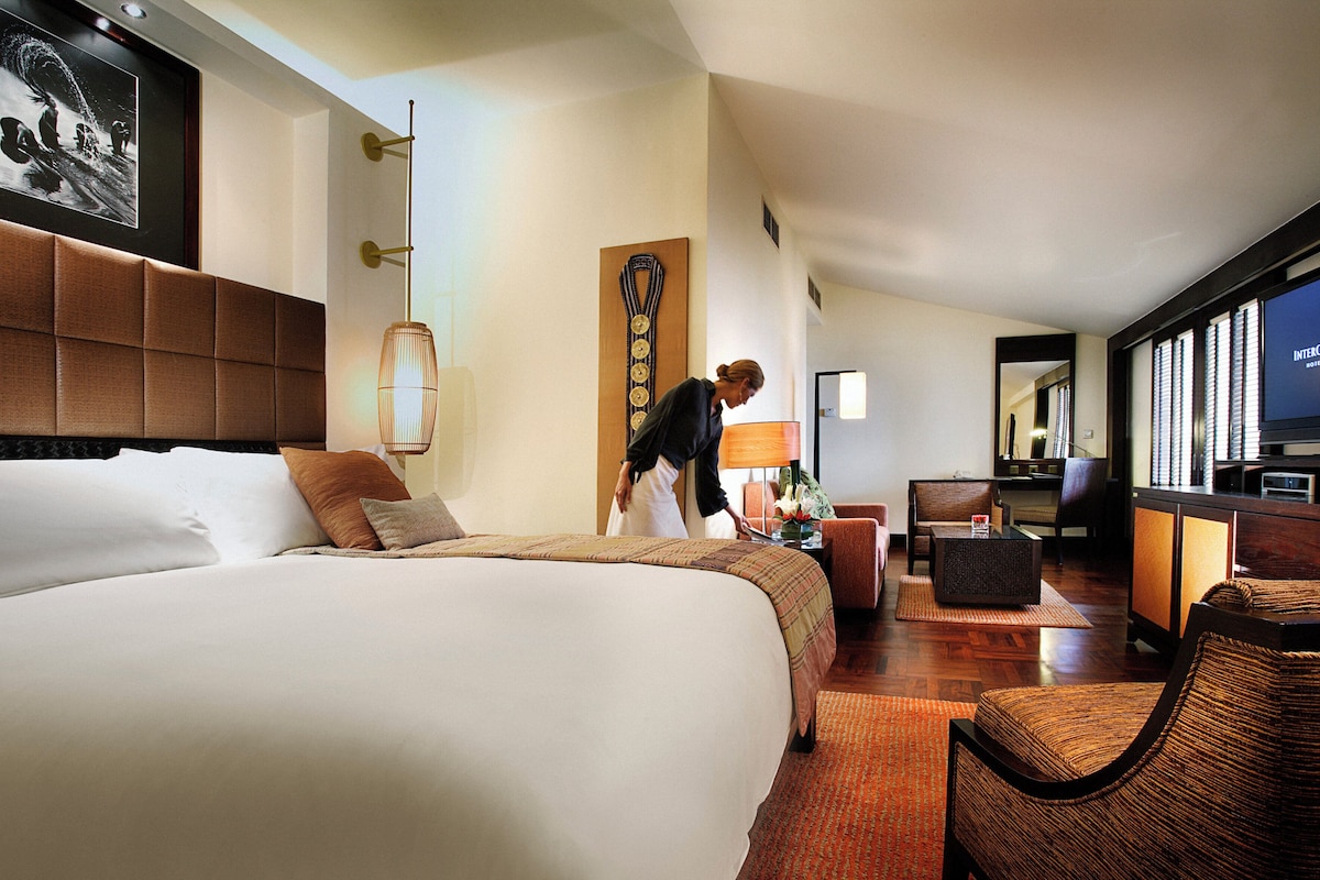 Een hotelkamer met een groot bed, een bureau met een televisie en een zithoek met stoelen.