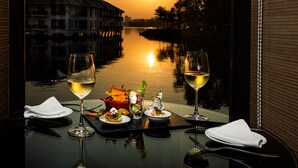 Una mesa con dos copas de vino blanco, un bol de ensalada y un plato pequeño de comida, con vistas a un río al atardecer.