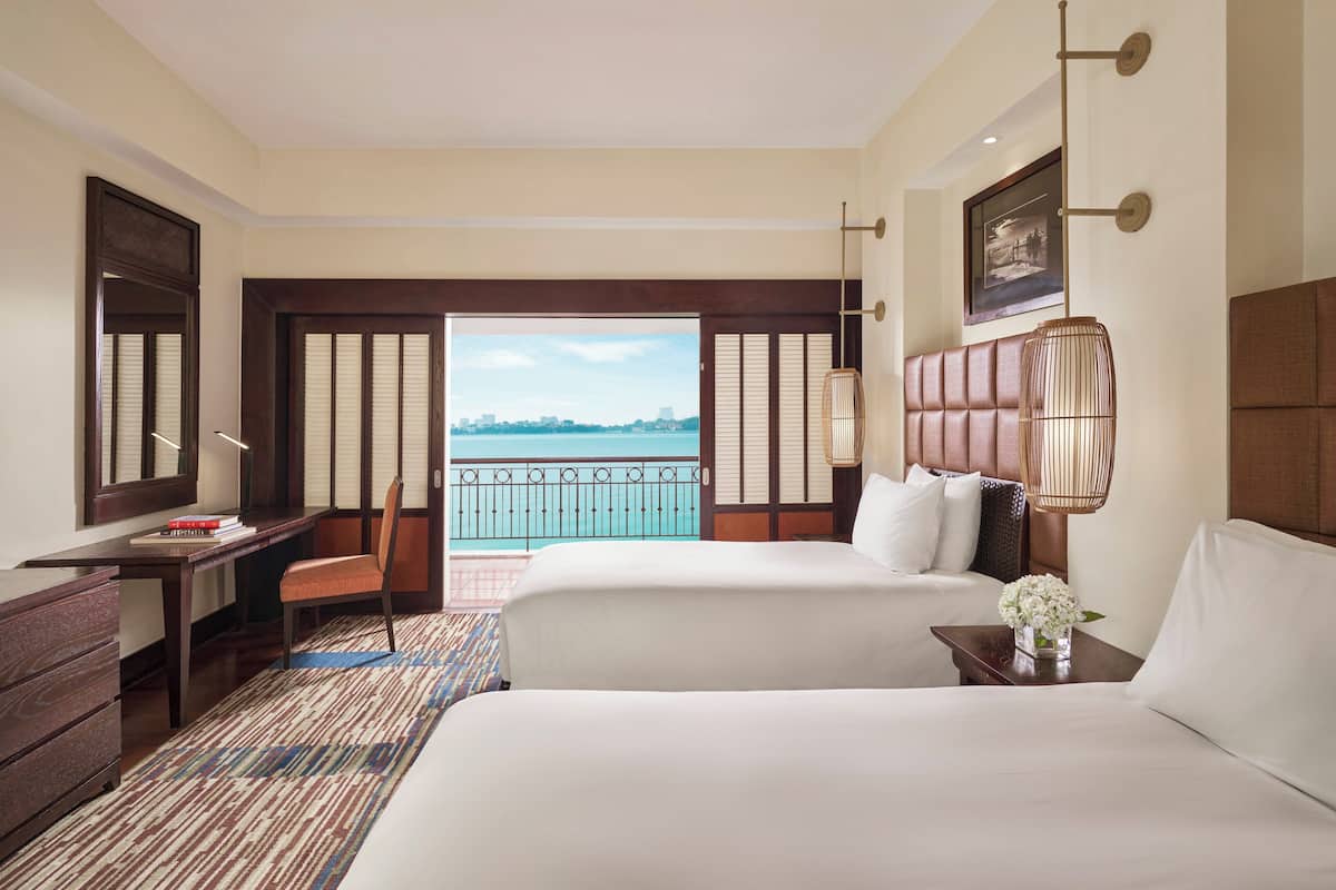 A hotel room with two beds, a desk, a chair, and a view of the sea.