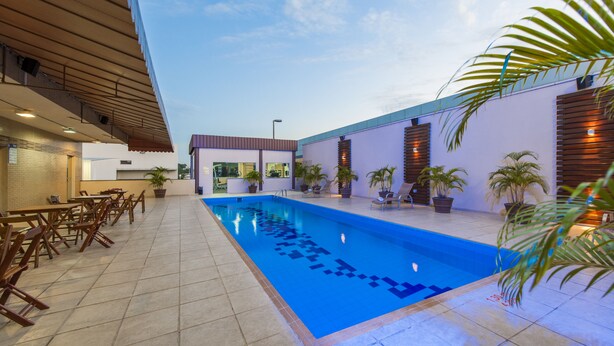 A swimming pool with a tiled deck, surrounded by lounge chairs and potted plants. - Sleep Inn Manaus (Manaus)