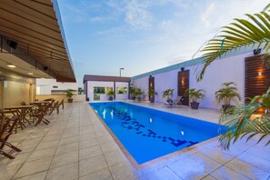 A swimming pool with a tiled deck, surrounded by lounge chairs and potted plants.
