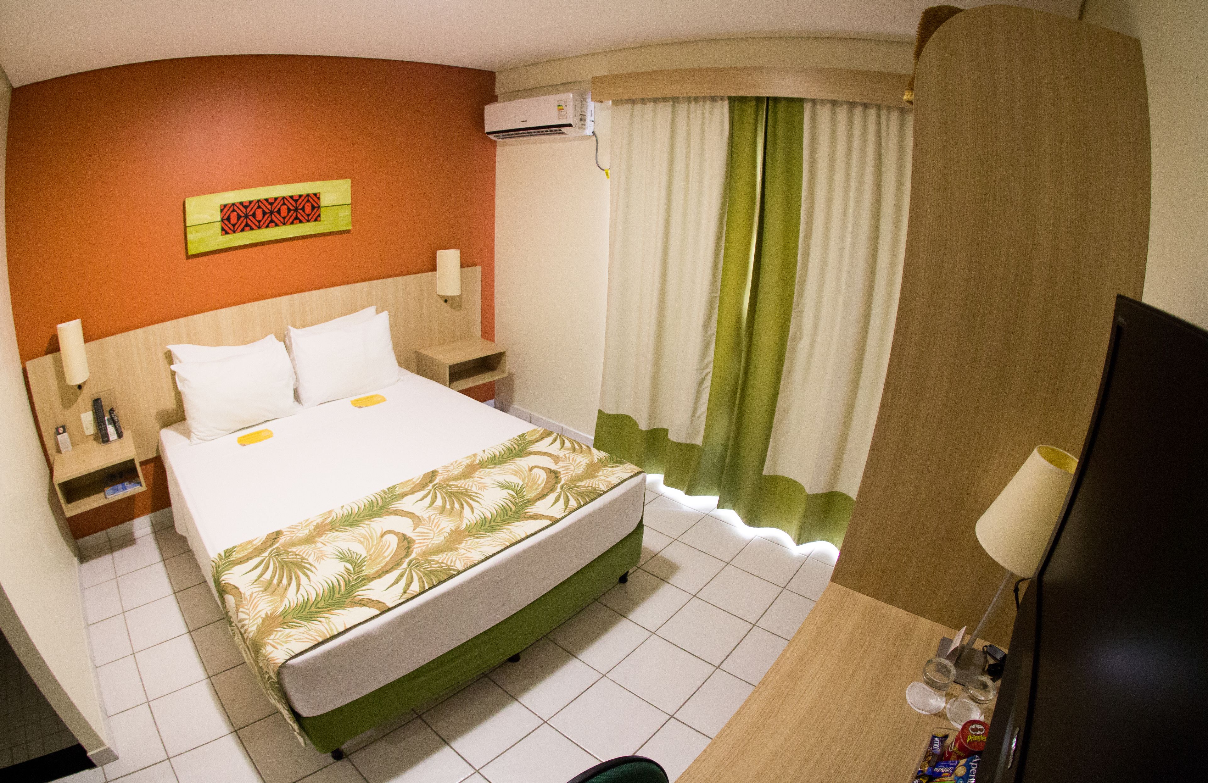 A hotel room with a bed, nightstands, a TV, and a bathroom area.
