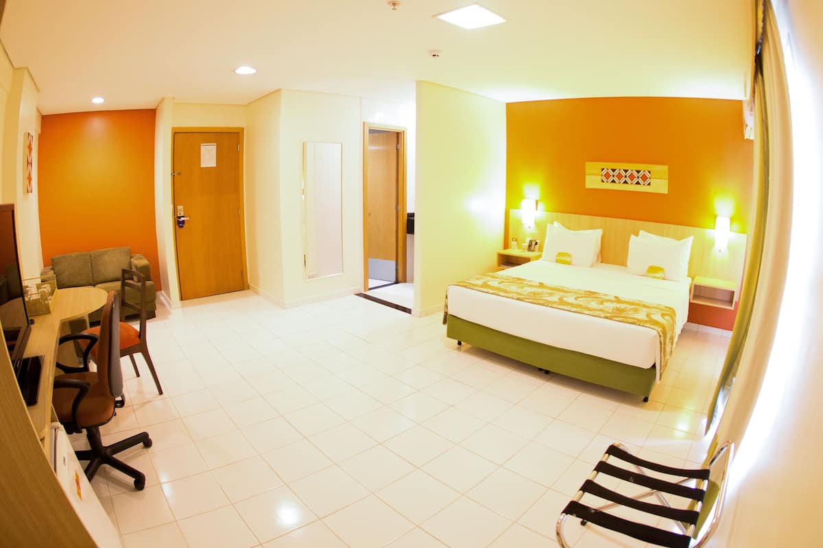 A hotel room with a bed, a desk with a chair, a small table, and a sofa.