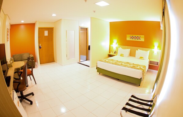 A hotel room with a bed, bedside tables, a desk with a chair, and a small seating area with a chair and a table.
