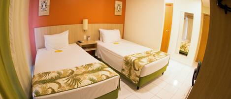Una habitación de hotel con dos camas, una mesita de noche, una lámpara y un espejo.