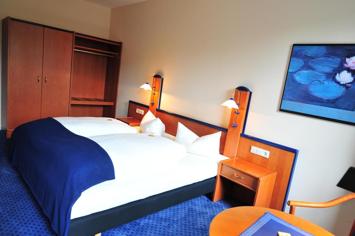 A hotel room with a large bed, two bedside tables with lamps, a wardrobe, and a painting on the wall.