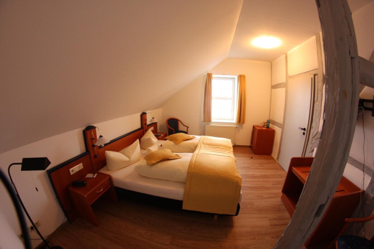 Un dormitorio con cama, mesitas de noche, lámpara, ventana con cortinas y radiador.