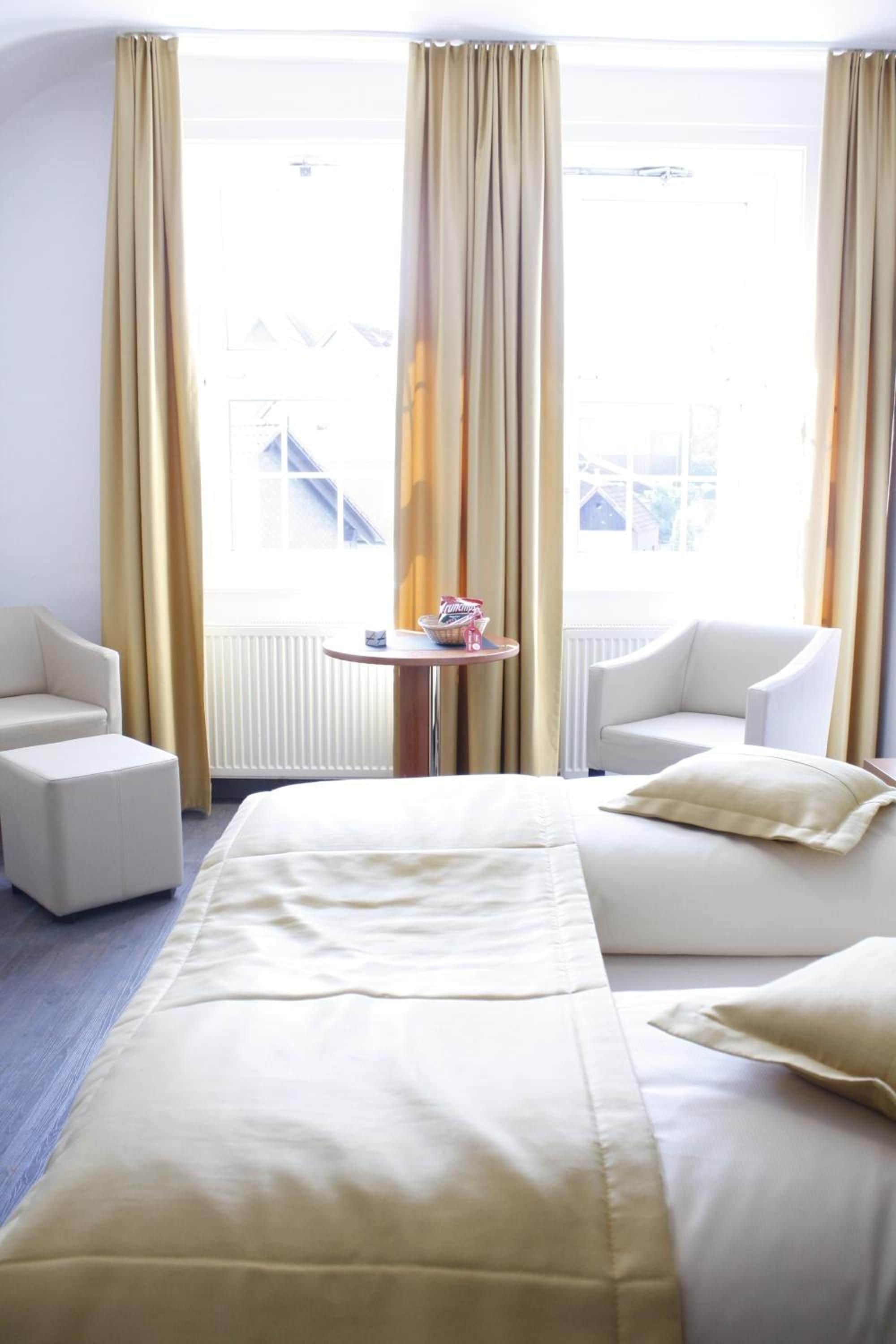 Ein Hotelzimmer mit einem Bett, zwei Sesseln, einem kleinen Tisch und Blick auf ein Gebäude.