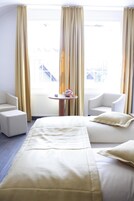 Habitación de hotel con una cama, dos sillones, una mesita y vistas a un edificio.