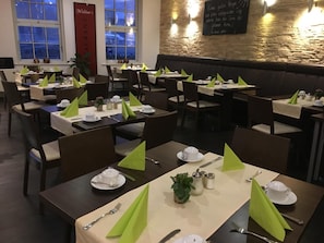 A restaurant with tables set for dining, featuring green napkins and white tableware.