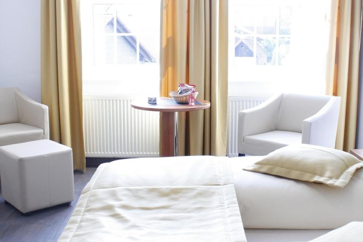 A hotel room with a bed, two armchairs, a small table, and a view of a building outside.