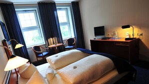 Quarto de hotel com duas camas, uma escrivaninha, uma cadeira, um abajur e uma televisão.