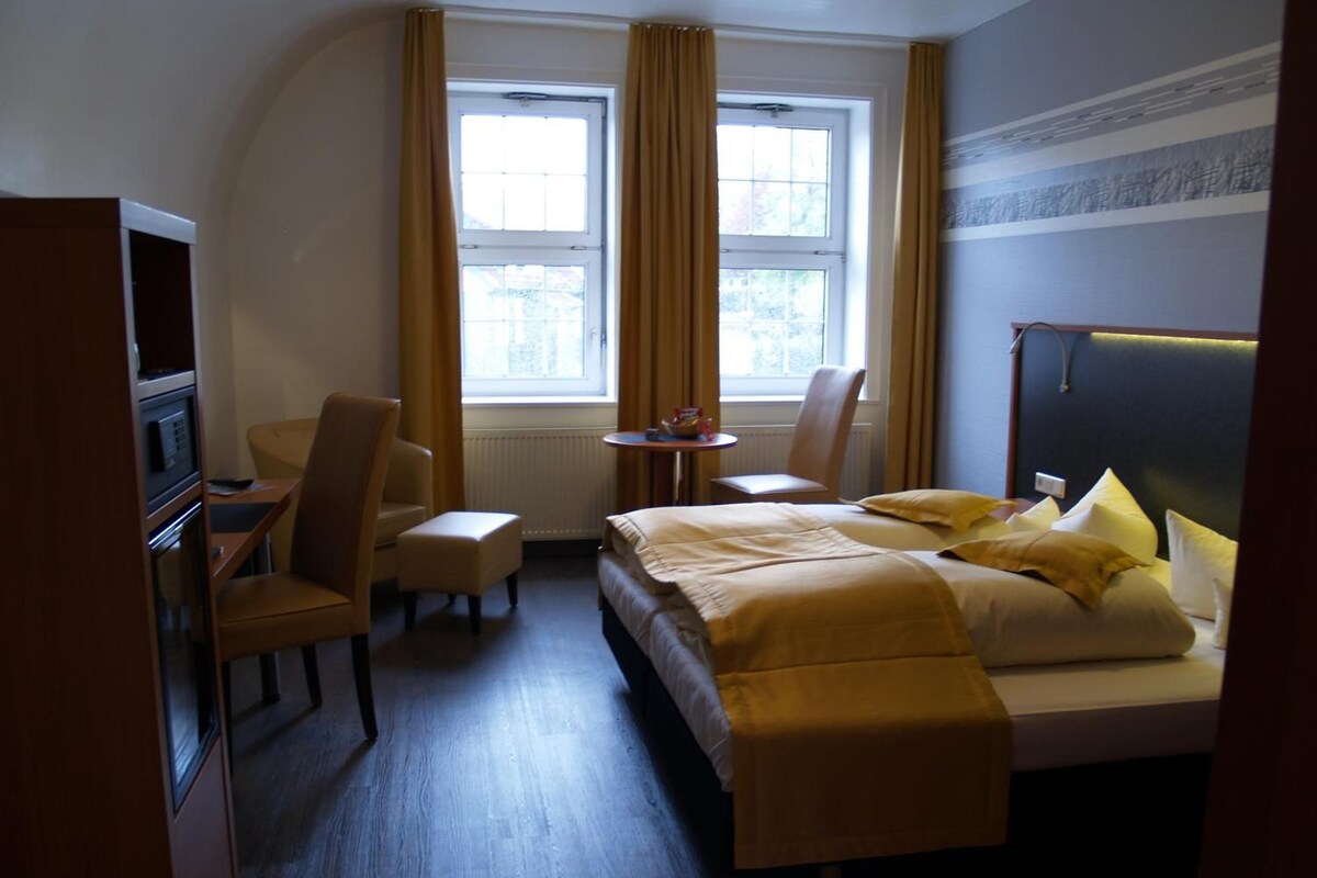 A hotel room with a bed, a desk, a chair, a small table, and a television.