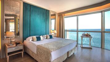Un dormitorio amplio con una cama grande, una mesita de noche, un espejo y vistas al mar a través de amplios ventanales.
