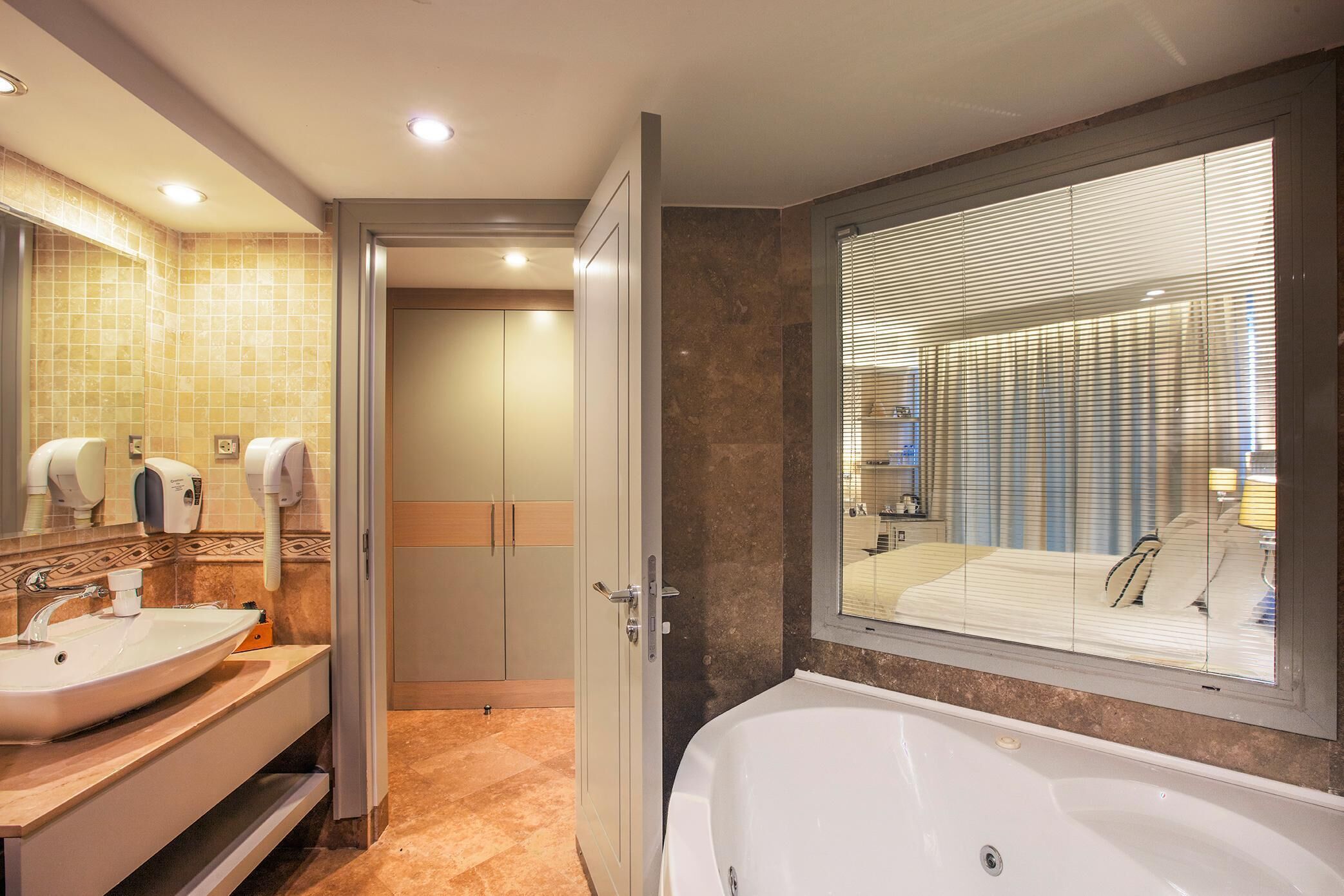 A modern bathroom with a large bathtub, a double sink vanity, and a mirror with built-in hand dryers.