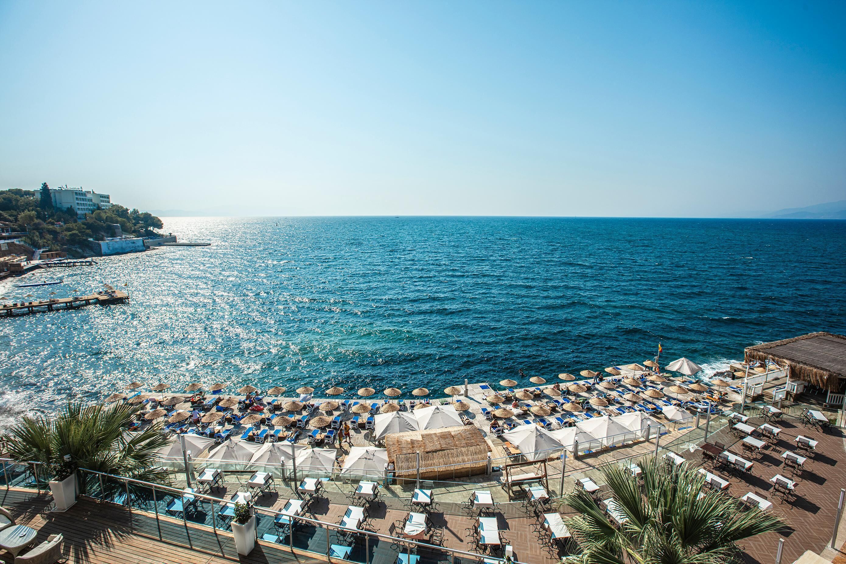 Un hôtel situé sur la côte, doté d’une terrasse en bord de mer avec des chaises longues, des parasols et une vue sur la mer.