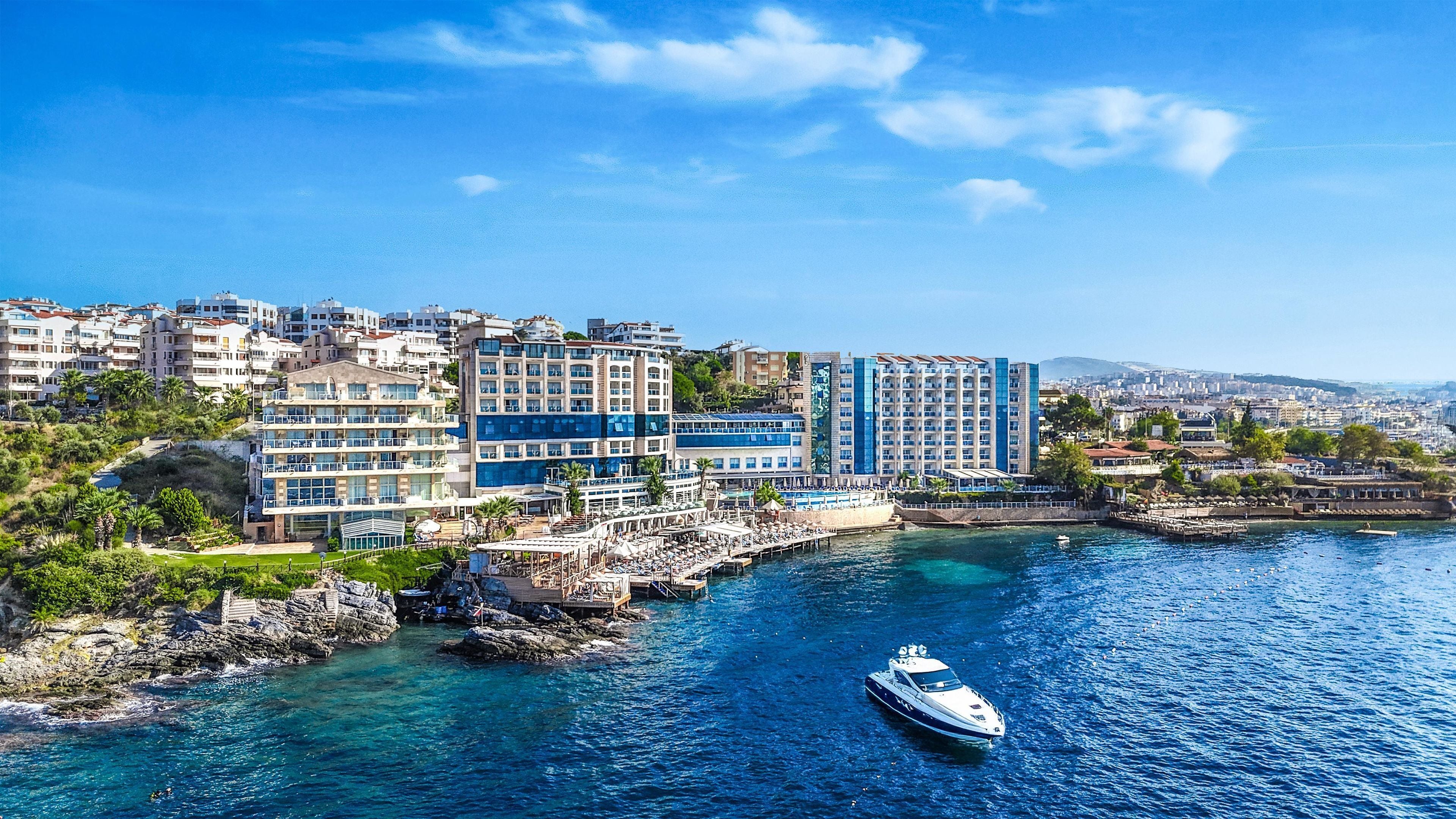 A coastal cityscape with modern buildings, a marina, and clear blue waters.