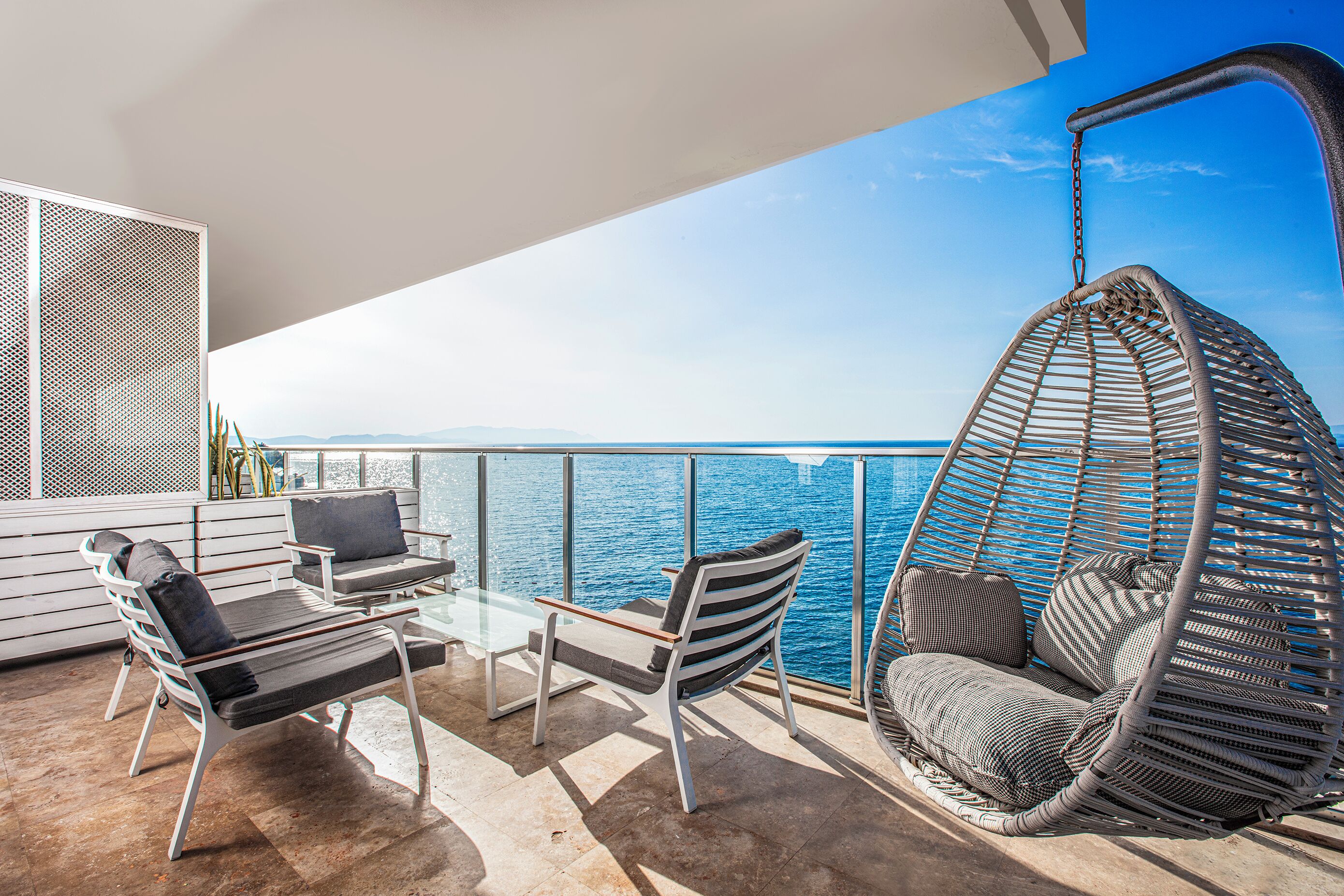A balcony with a hanging chair, a sofa, and a table with chairs.