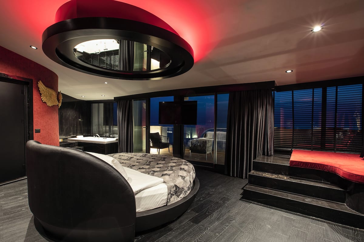 Un dormitorio moderno con una cama redonda, un espejo grande y vistas de la ciudad a través de las ventanas.