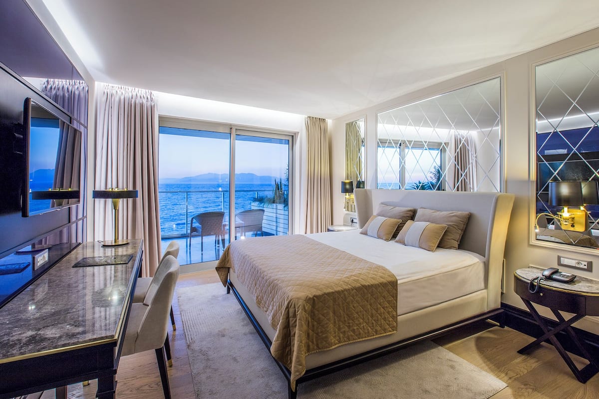 Una habitación de hotel con una cama grande, un escritorio con una silla, un televisor y un balcón con vista al mar.