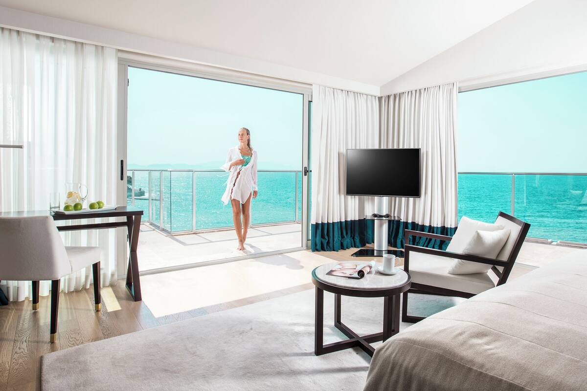 Habitación de hotel con una cama grande, un escritorio, un televisor y un balcón con vistas al mar.