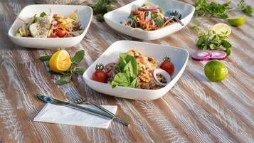 A table with various dishes and a wicker chair, set against a backdrop of a blue ocean view.