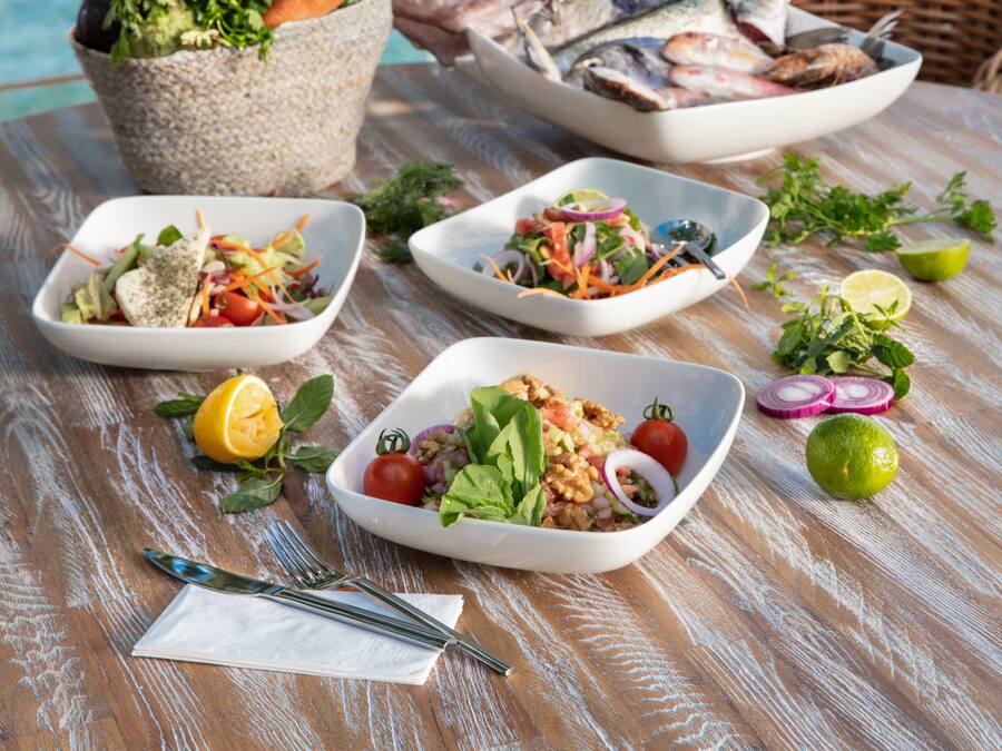 A table with various dishes and a wicker chair, set against a backdrop of a blue ocean view.