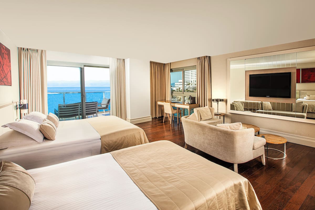 Habitación de hotel con dos camas, un sofá, un televisor y un balcón con vistas al mar.