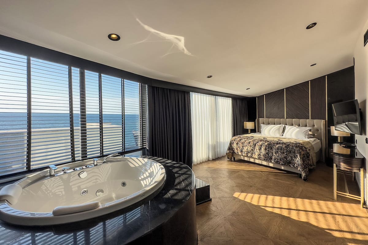 Una habitación de hotel moderna con una cama grande, una zona de estar con vistas al mar y un jacuzzi.