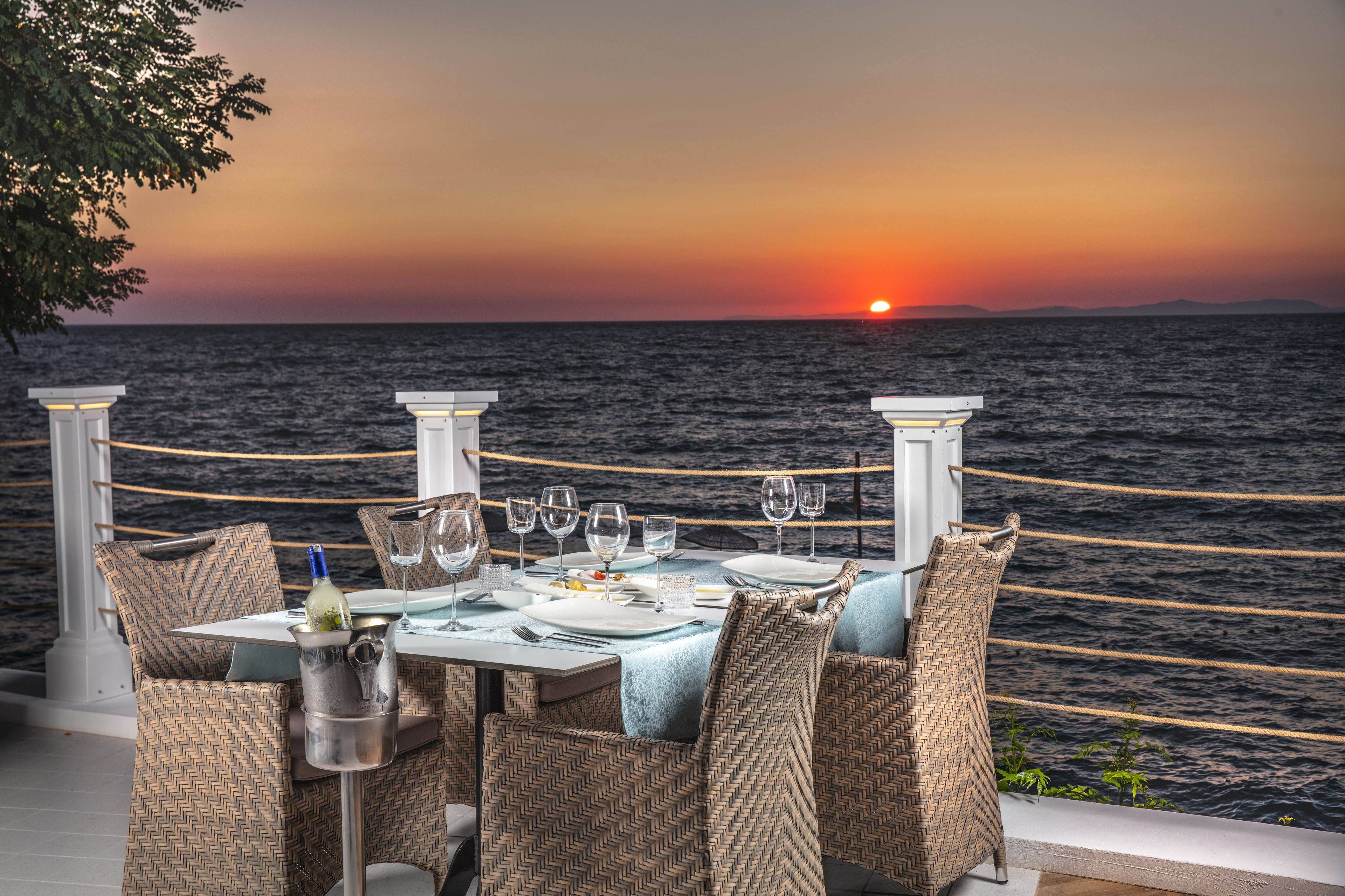A table set for four with a view of the sunset over the sea.