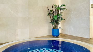 A circular indoor pool with a blue and white tiled pattern, surrounded by beige tiled walls and a wooden floor.