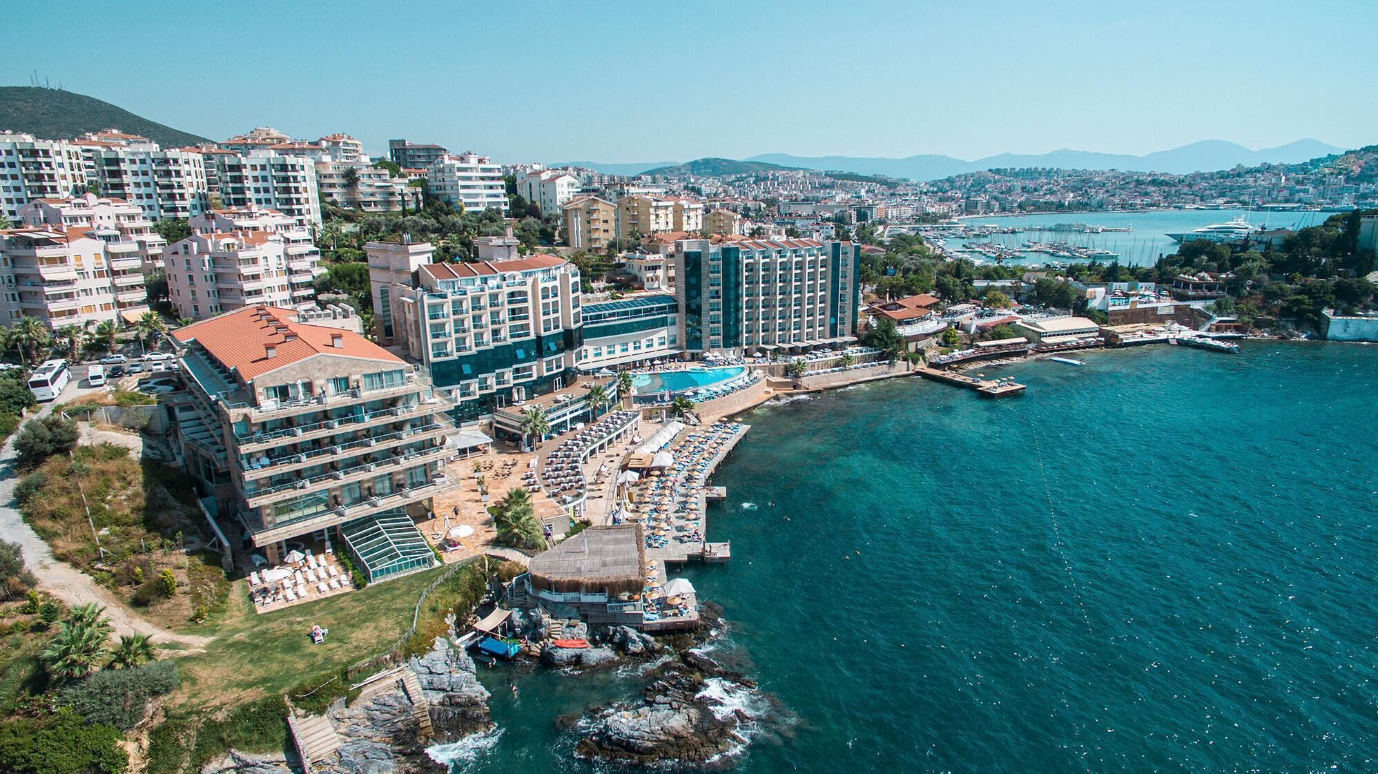 An aerial view of a coastal hotel with multiple buildings, a swimming pool, and a rocky shoreline.