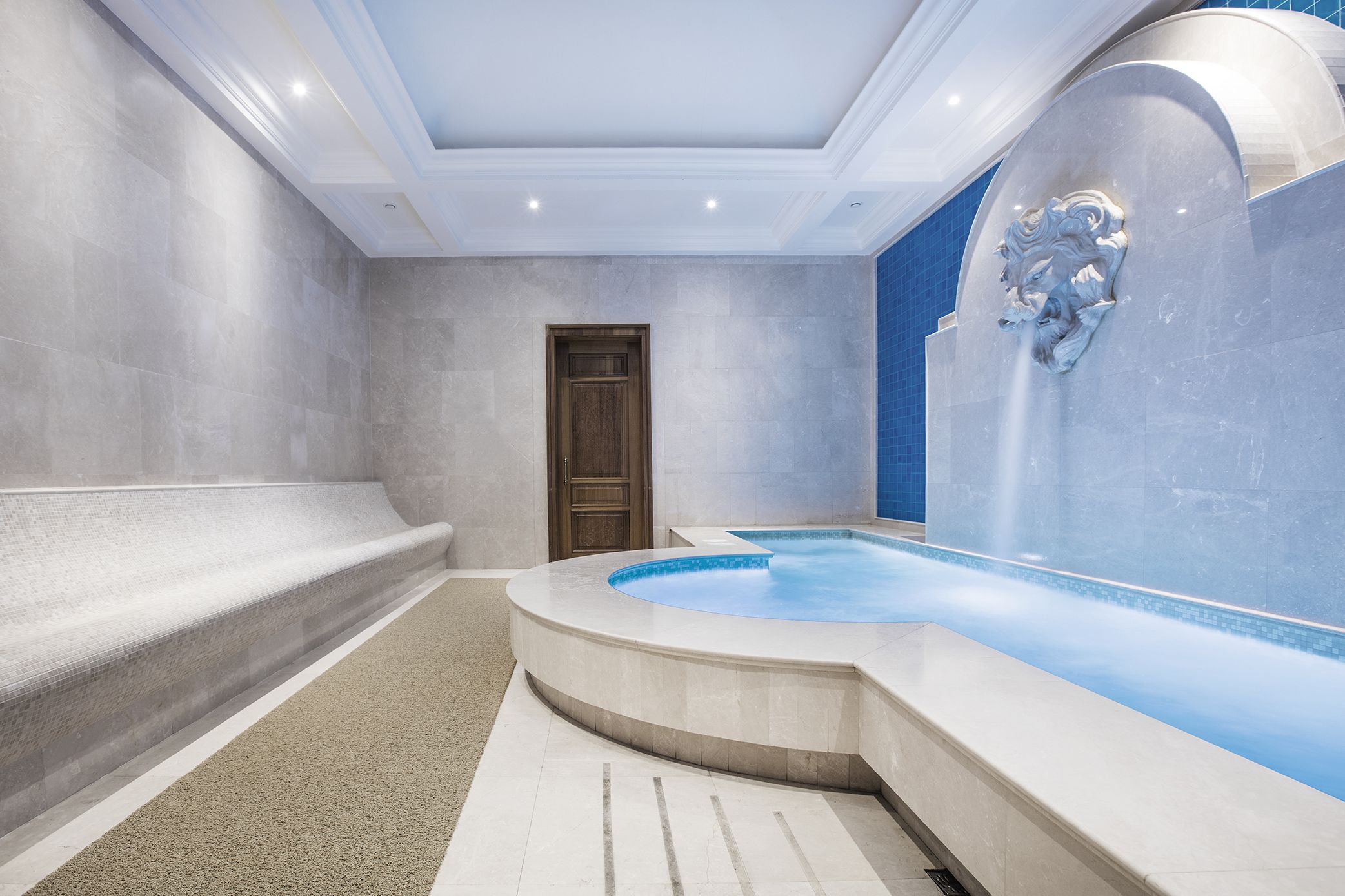 Un moderno espacio de spa con pared de piedra, puerta de madera y piscina con borde de mosaico azul.