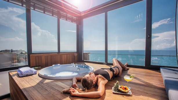 A woman relaxing on a wooden deck with a hot tub and a drink, overlooking the sea. - Charisma De Luxe Hotel (Kusadasi)