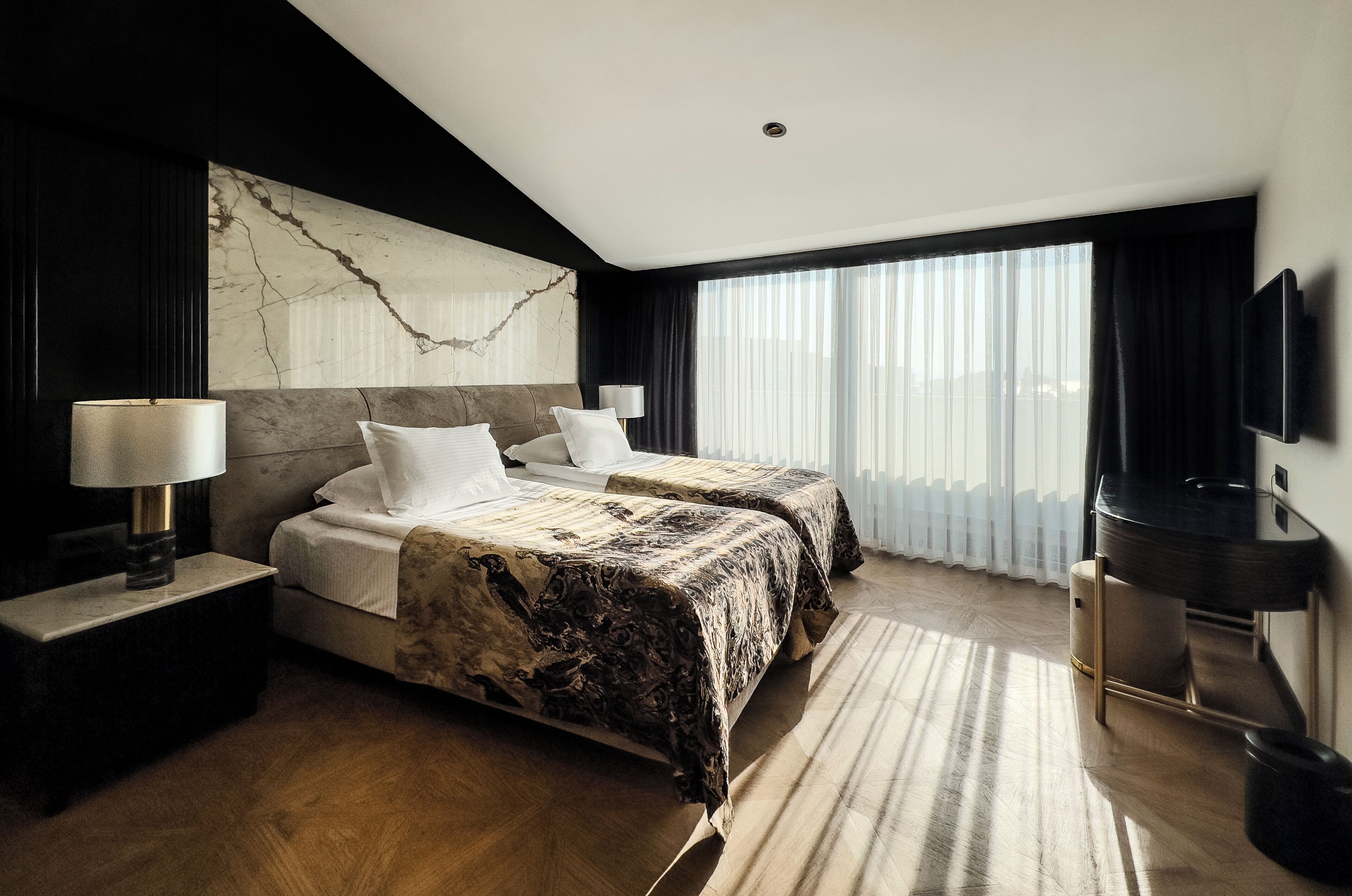 A modern hotel room with two beds, a large marble wall, a flat-screen TV, and a large window with curtains.