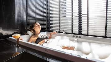 Una persona descansando en una bañera moderna con una bebida al lado.
