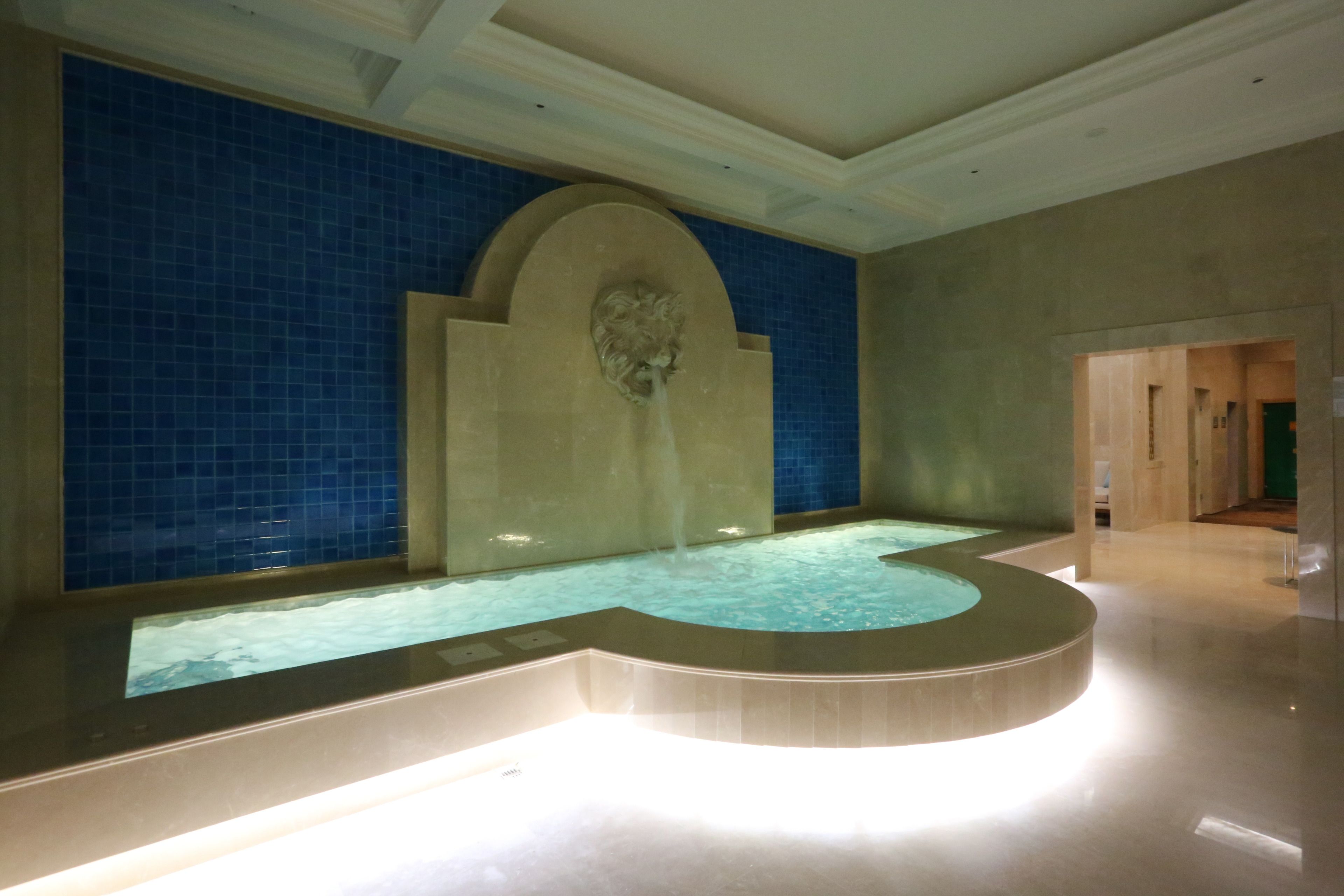 Ein großzügiges Hallenbad mit gewölbter Kante, umgeben von blautönen Kacheln und einem Steinbogen.