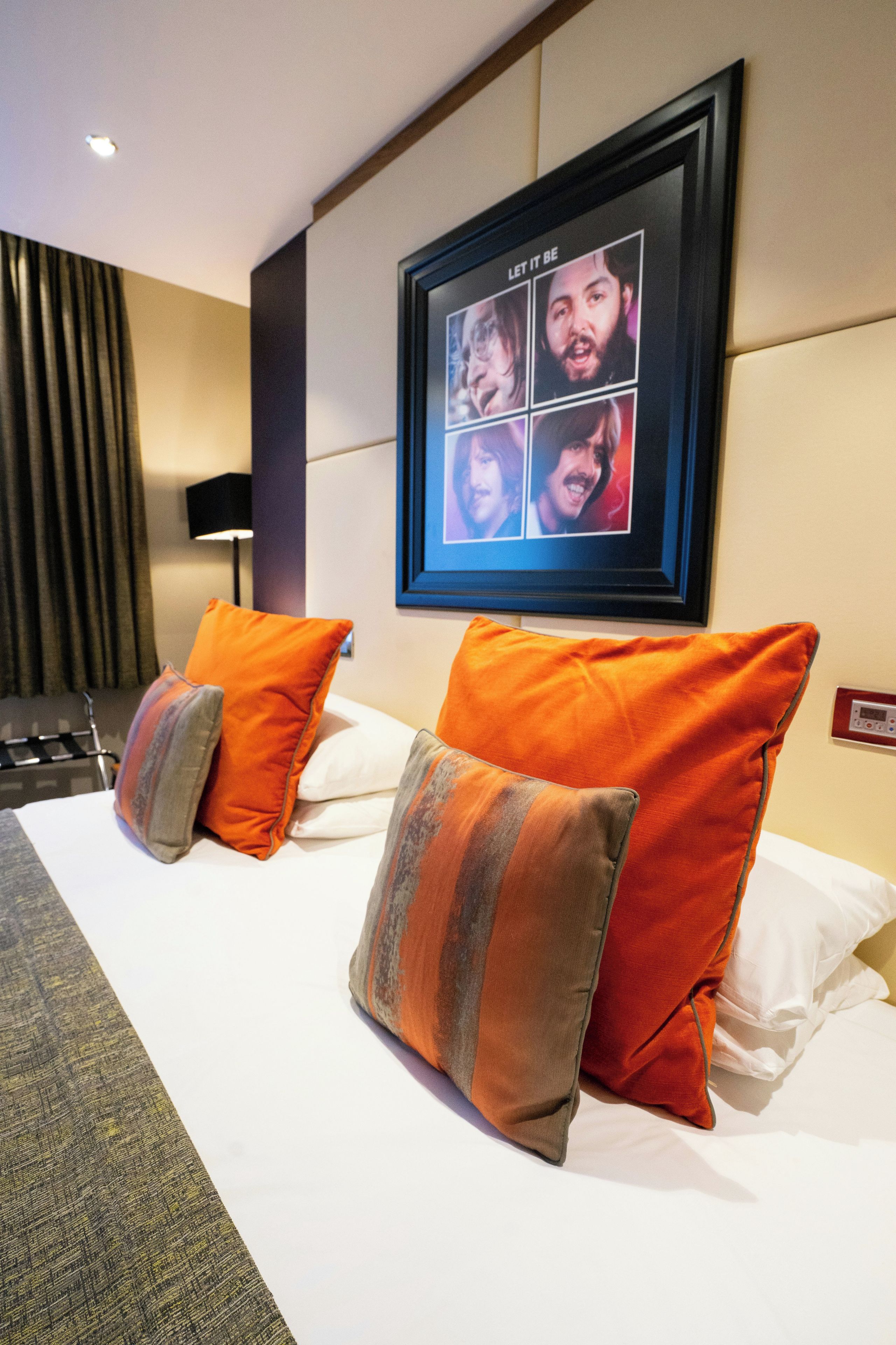 A hotel room with a bed, two pillows, a wall-mounted picture frame, and a lamp.