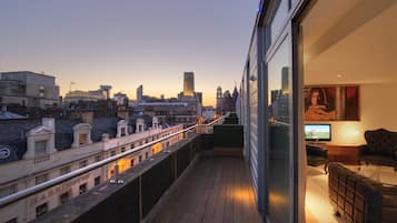 Un balcón con vista a la ciudad, televisión y zona de estar con sofá y sillón.