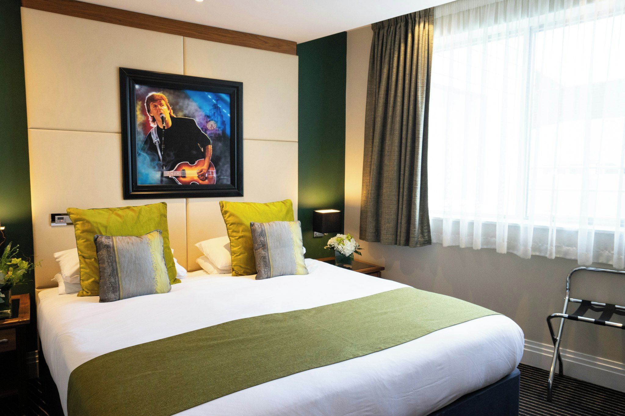 A hotel room with a large bed, a framed picture on the wall, a nightstand, and a window with curtains.