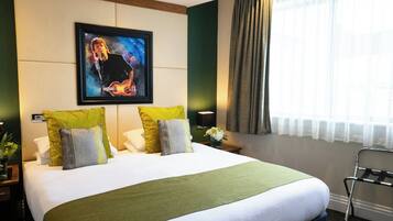 A hotel room with a large bed, a framed picture on the wall, a nightstand, and a window with curtains.