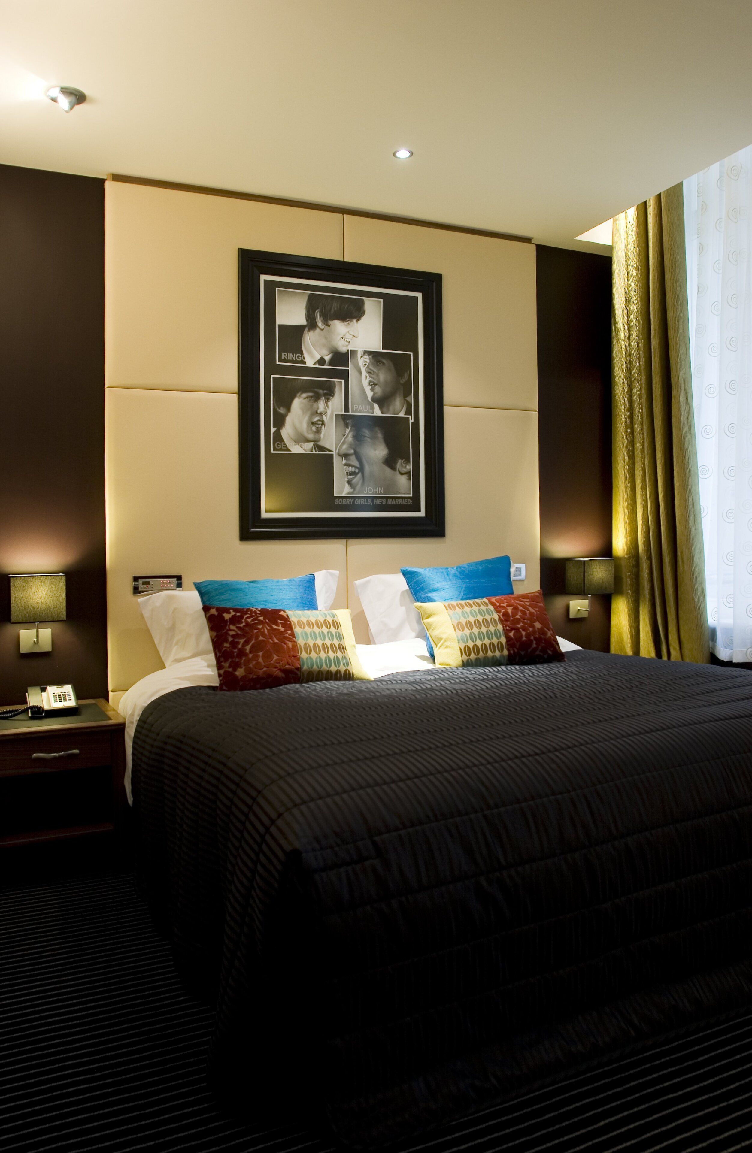 A hotel room with a large bed, a framed photo on the wall, and a bedside table with a phone.