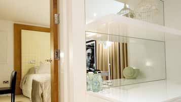 Un dormitorio moderno con un espejo grande, una cama, una silla y una pequeña mesa con botellas y vasos.