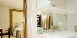 A modern bedroom with a large mirror, a bed, a chair, and a small table with bottles and glasses.