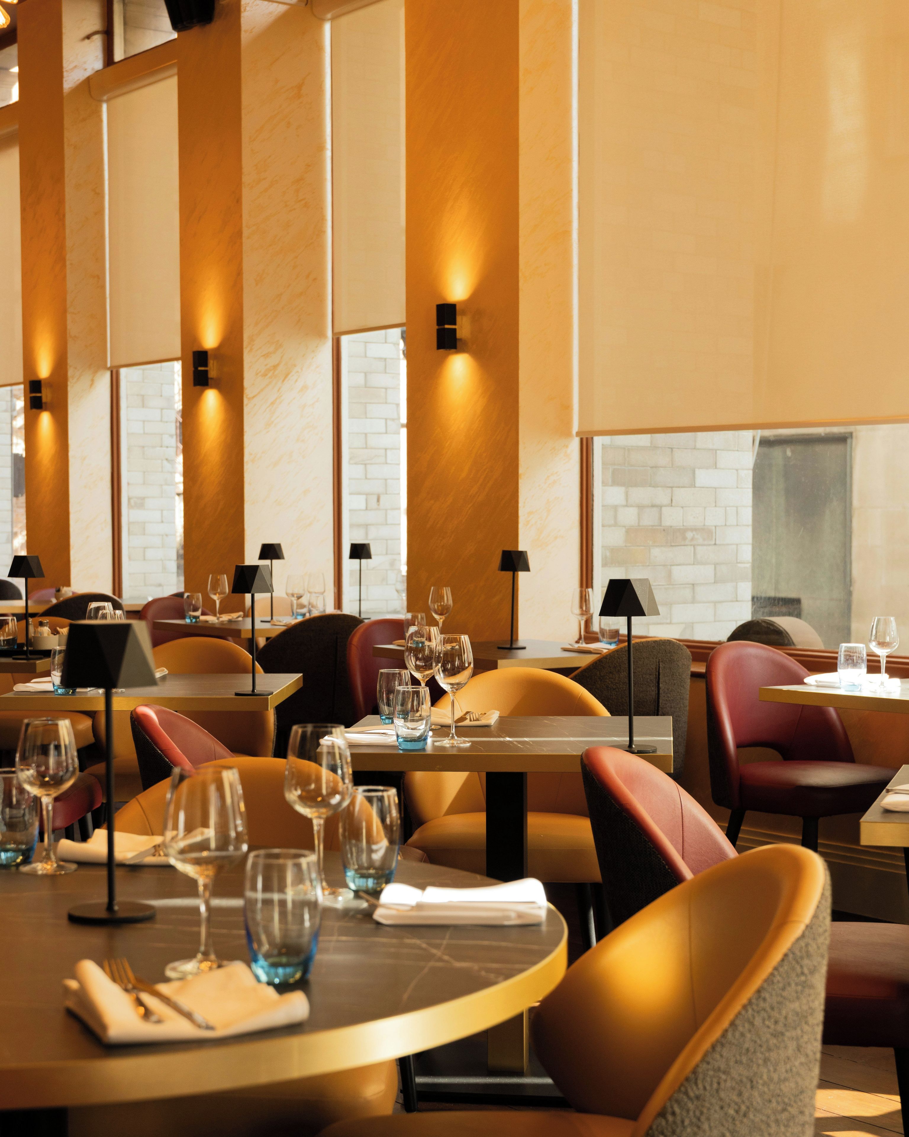 Un interior de restaurante con mesas redondas, sillas y copas de vino.