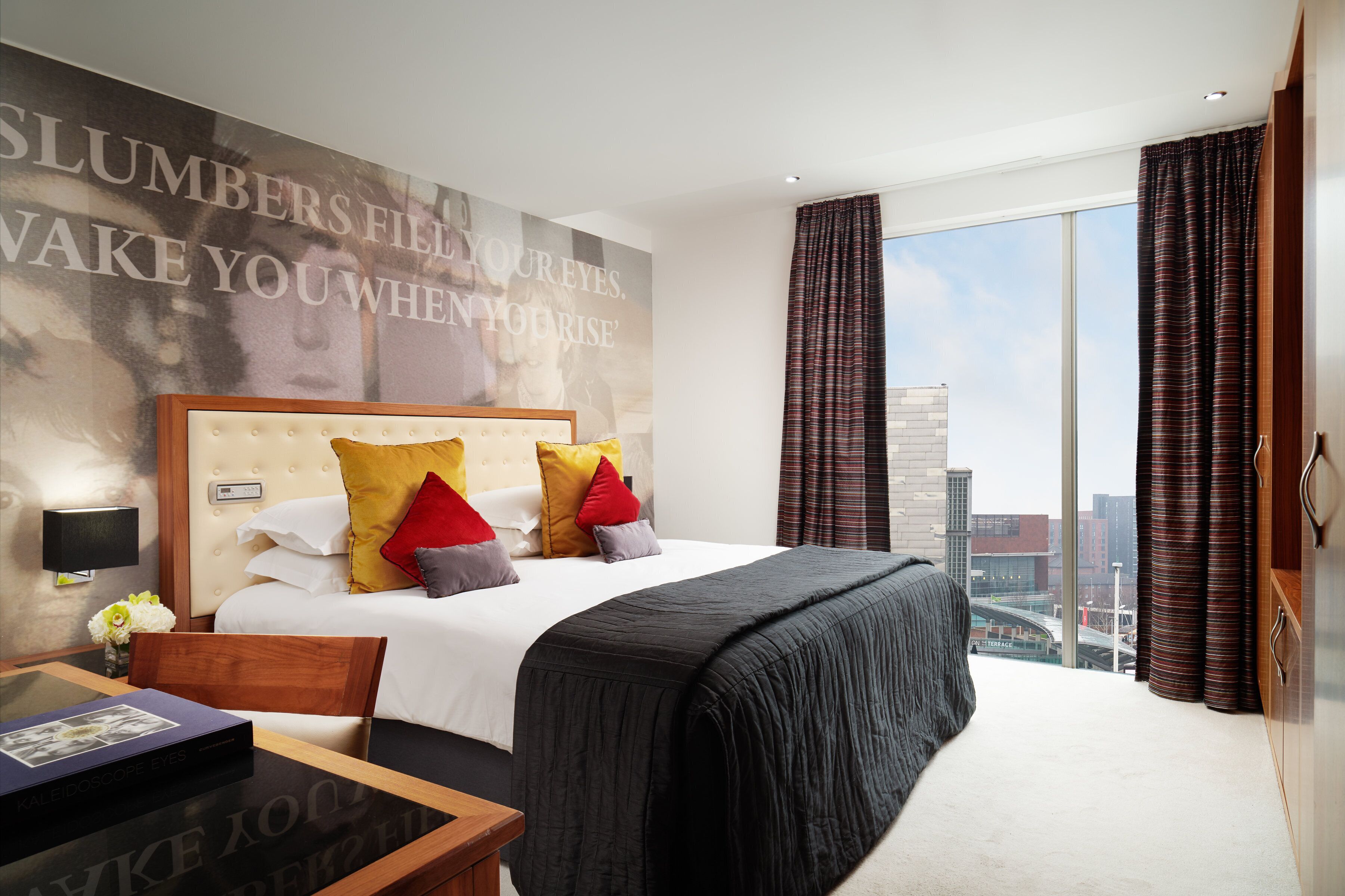 Habitación de hotel con una cama grande, vistas a la ciudad, diseño moderno y un cartel motivacional en la pared.