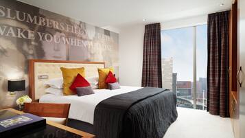 Habitación de hotel con una cama grande, vistas a la ciudad, diseño moderno y un cartel motivacional en la pared.